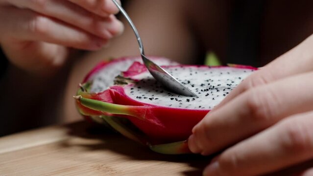 A young woman is eating the white flesh of the Dragon fruit with a spoon. Close-up, in slow motion.