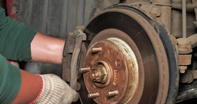 A man in a garage removes a brake pad from a disc. A man is replacing an old brake pad with a new one in his garage. A man repairs brakes on a car in a workshop.Car repair concept.