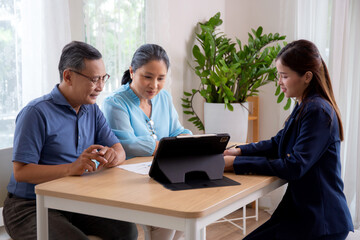 Young asian woman counseling to elderly couple husband and wife about insurance life for planning in living room at home, insurance life agent or consultant explaining with senior for decisions.
