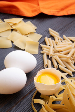 variety of types and shapes of italian pasta on dark wooden table with ingredients, flour and eggs. dry pasta background. close up