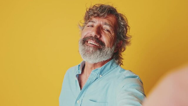 Happy elderly gray-haired man looking camera taking selfie , isolated on an orange background