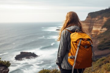A girl traveler of European appearance, with a backpack, looks at the sea