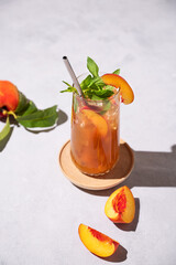 Refreshing peach tea with ice and mint. Homemade cold summer drink on a light background with fresh fruits and shadows. Top view