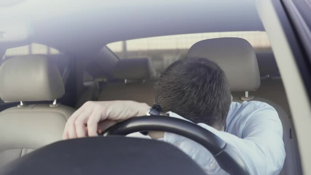 A man grabs his head with his hands in severe frustration. A man in severe emotional stress after a hard day at work gives vent to his emotions while sitting in a car