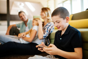 Young Caucasian boy playing video games on the smartphone in the living room at home