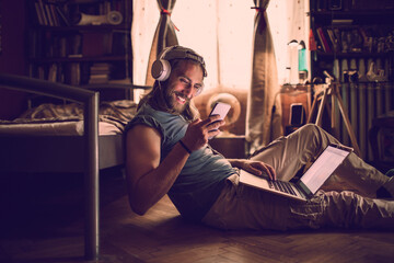 Young man using a smartphone while listening to music in his bedroom at home