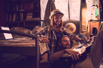 Young couple playing the guitar and singing together in the bedroom at home