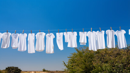 Clothesline, rope with clean white clothes during sunny summer day against blue sky.