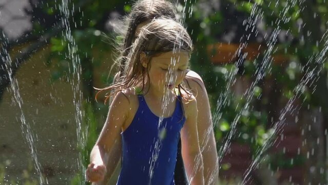 Long-haired girls are jumping in the water jets from a revolving water sprinkler