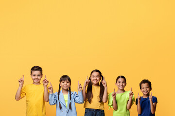 Happy multiracial children pointing up at copy space, yellow background