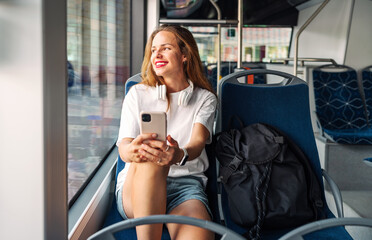 Young urban woman sitting in public city electric bus and smiling.