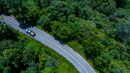 Aerial top view road in forest with car motion. Winding road through the forest. Car drive on the road between green forest. Ecosystem ecology healthy environment road trip.