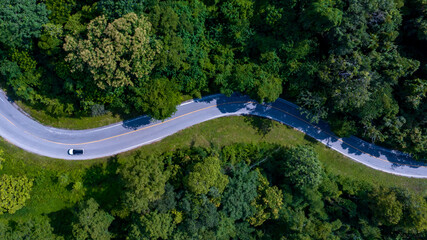 Aerial top view road in forest with car motion. Winding road through the forest. Car drive on the road between green forest. Ecosystem ecology healthy environment road trip.