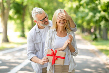 Romantic Surprise. Loving senior man covering wife's eyes and giving gift outdoors