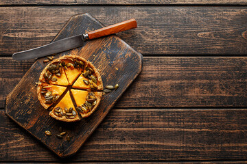 Colorful mini pumpkin tart decorated with roasted pumpkin seeds on rustic wooden board with vintage knife. Overhead view, copy space