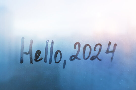 lettering Hello and numbers 2024 of new year paint with finger on splashed by rain foggy glass on blue sunset window
