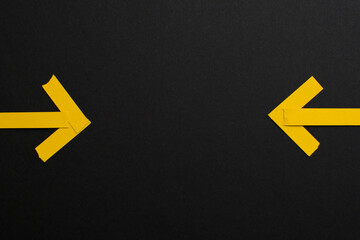 Two yellow paper arrows on black background pointing at middle empty space