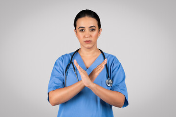 Serious latin female doctor surgeon in blue uniform crossed arms, making stop sign, standing...