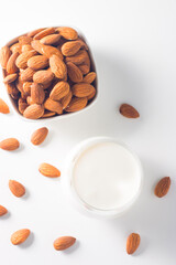 Organic almond milk in glass with raw almonds on white table 