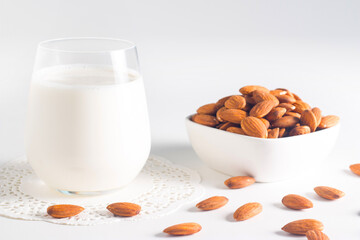 Organic almond milk in glass with raw almonds on white table 