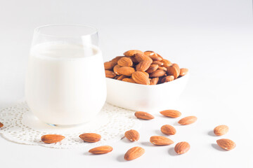 Organic almond milk in glass with raw almonds on white table 