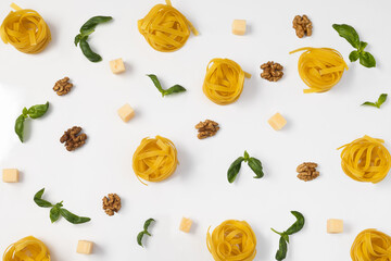 Pattern of pesto ingredients (nuts, cheese, basil, pasta) on a white background, top view