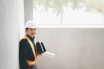 A foreman wearing a hard hat stands holding a blueprint. Supervising and inspecting the construction project of the building to be successful as planned.