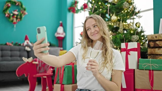 Young blonde woman celebrating christmas make selfie by smartphone drinking champagne at home