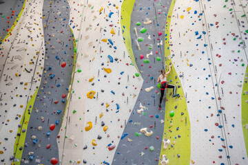 Rock climber young woman hanging on colored hooks on climbing artificial wall indoors of sport centre of Prague. Extreme sports and bouldering concept