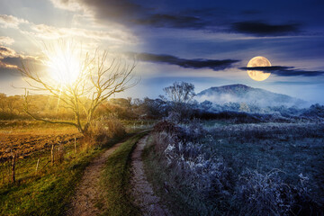 Naklejka na ściany i meble rural landscape with country road to mountain through agricultural fields behind fence and few trees in late autumn foggy weather with sun and moon at twilight. day and night time change concept