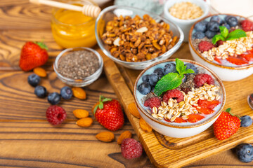 Bowl of granola with yogurt and fresh berries on a texture table. Yogurt berries, acai bowl, spirulina bowl. Healthy food, balanced breakfast. Strawberries, blueberries, kiwi, peach, almonds and chia.