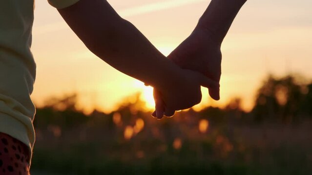 Mom and child holding hands together on sunset time. Silhouette as kids takes mother hand. close up
