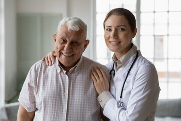 Portrait of smiling young female nurse or caregiver posing with happy senior 80s male patient, attentive woman doctor hug support, give good help to mature 70s man, elderly healthcare concept