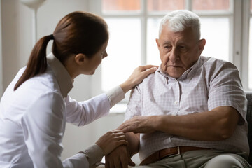 Caring female nurse or doctor talk support upset lonely mature 80s male patient in retirement...