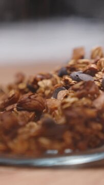 Vertical video. They transfer the freshly prepared homemade granola into a jar, slow motion, the grains scattering.