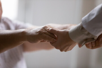 Close up of female caregiver hold hands help stand up sick disabled senior male patient in...
