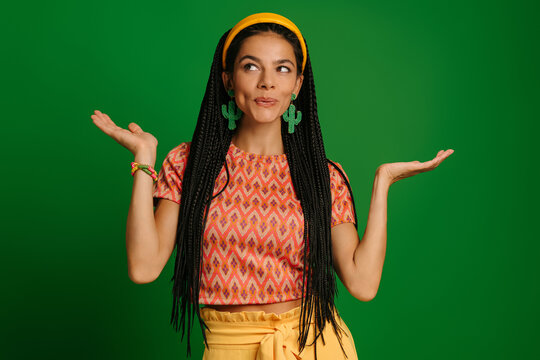 Attractive young Mexican woman looking uncertain while gesturing against green background