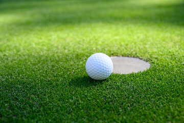 Closeup of white golf ball next to the cup on a putting green

