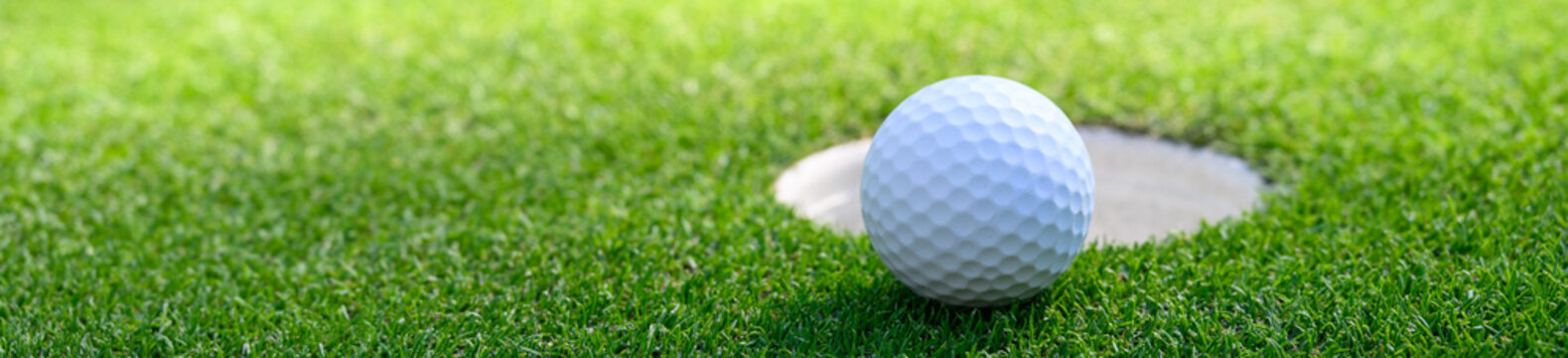 Closeup of white golf ball next to the cup on a putting green
