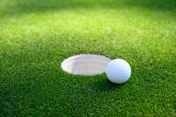 Closeup of white golf ball next to the cup on a putting green

