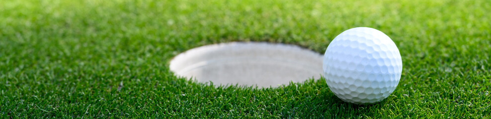 Closeup of white golf ball next to the cup on a putting green
