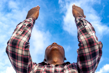 A powerful image of a pastor, palms up, his figure against the serene blue sky, as he prays with...