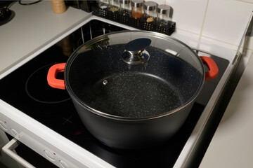 Empty saucepan with marble coating inside and glass lid on induction ceramic hob for cooking