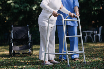 Asian young woman nurse at nursing home take care disabled senior man. Caregiver doctor serve physical therapy for older elderly patient to exercise and practice walking on walker or cane at backyard.