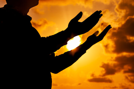 An inspiring photograph showing the silhouette of a man, his arms outstretched towards the breathtaking sunset of the solstice, immersed in heartfelt prayer.