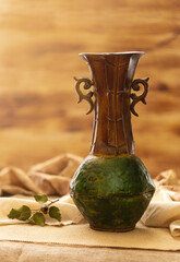 Still life of brass amphora vase with two handles. Base is green and rest brown. There are some...