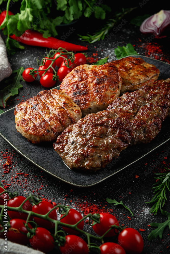 Sticker Grilled meat and chicken cutlets in a dark rectangular plate on the table with spices, vegetables, herbs and onions.