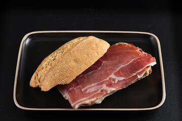 Serrano ham sandwich on dark tray, all isolated on a black background