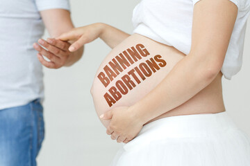 A pregnant woman holds her husband's hand on her stomach with the inscription - BANNING ABORTIONS.