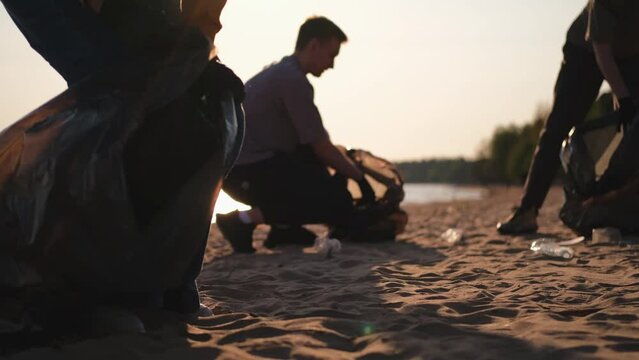 Earth day. Volunteers activists collects garbage cleaning of beach coastal zone. Woman and mans puts plastic trash in garbage bag on ocean shore. Environmental conservation coastal zone cleaning